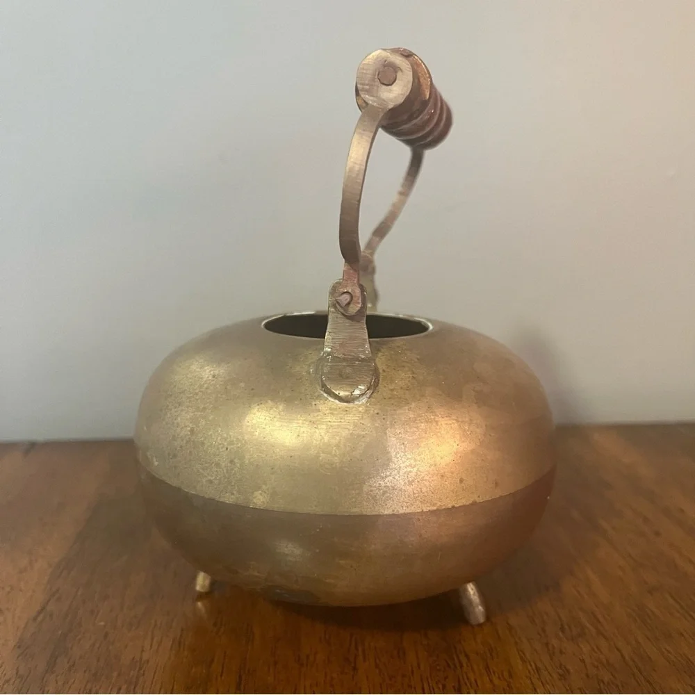 antique brass kettle with a wooden handle and three-legged base.